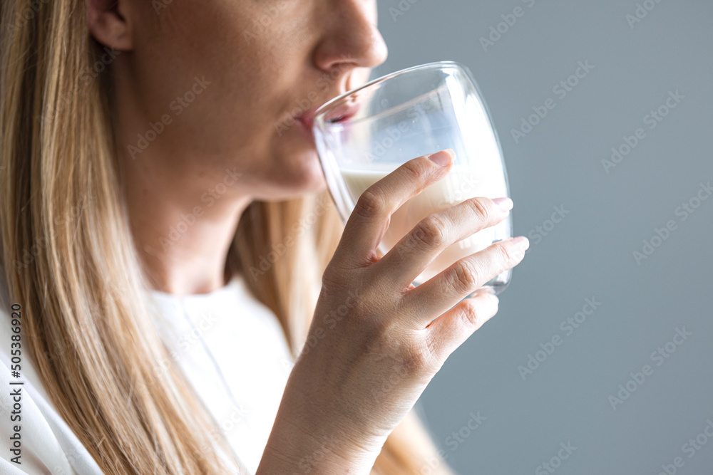 Young woman drinking a glass of milk. Attractive and amazing girl stands in kitchen at table and drinking milk. Girl enjoyes the moment. Woman drinking fresh milk on white background