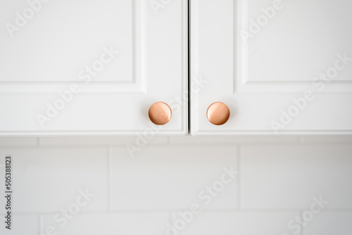Two small round copper door knob on white kitchen cabinet
