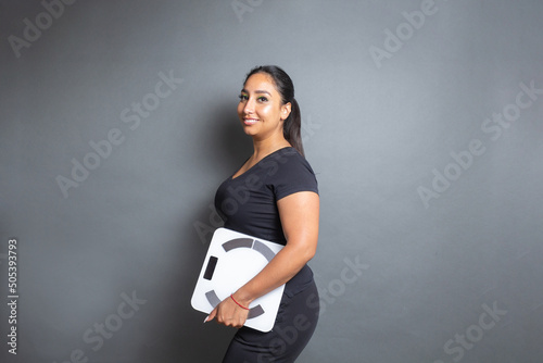 young business woman looking at camera holding body scale