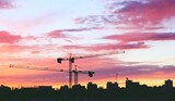 Grúas torre de construcción al atardecer en el barrio de Montecarmelo, Madrid, España. Silueta de las grúas y de los edificios del barrio bajo un bonito cielo rosa y violáceo.
