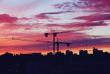 Grúas torre de construcción al atardecer en el barrio de Montecarmelo, Madrid, España. Silueta de las grúas y de los edificios del barrio bajo un bonito cielo rosa y violáceo.