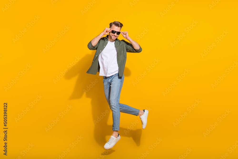 Full length body size view of attractive cheerful guy jumping touching specs stroll isolated over bright yellow color background Full length body size view of attractive cheerful guy jumping touching specs stroll isolated over bright yellow color background
