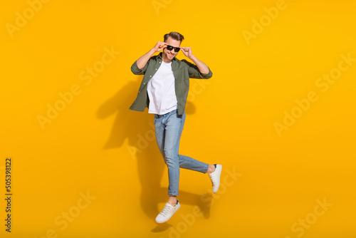 Full length body size view of attractive cheerful guy jumping touching specs stroll isolated over bright yellow color background