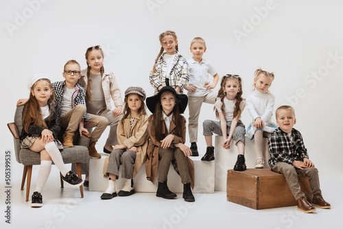 Group of beautiful kids, little girls and boys in modern outfits posing on grey studio background. Beauty, kids fashion, education, happy childhood concept.