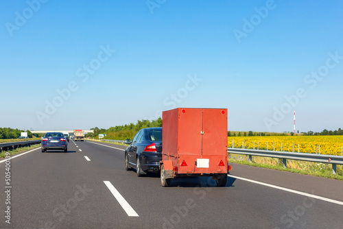 Black car with red carry-on cargo trailer on the highway.