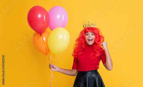 shocked child in crown with party balloon on yellow background
