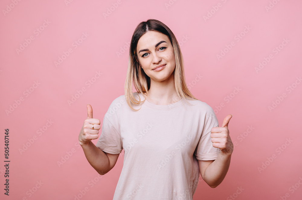 A girl in casual clothes shows thumbs up with both hands and smiles cutely on an isolated background A girl in casual clothes shows thumbs up with both hands and smiles cutely on an isolated background