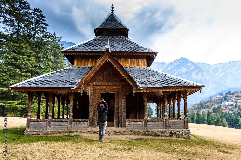 Young woman worshipping in Shangchul mahadev temple in the meadow of Shahgarh, surrounded by Deodar Tree and Himalayas mountains in Sainj Valley, Great Himalayan National Park, Himachal Pradesh, India
