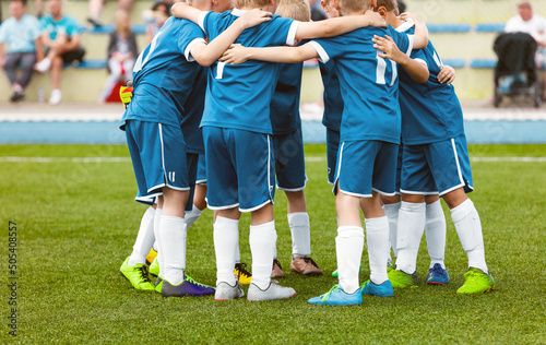 Motivated youth soccer team cheering on court. Players huddling in a circle on the field. Football captain talking to a group of soccer players. Happy football team in a circle
