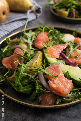 closeup of healthy avocado, salmon, and arugula salad on a plate