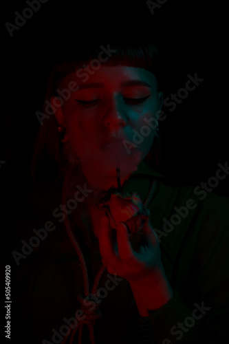 A gothic girl smoking a flower pipe with smoke and dark background