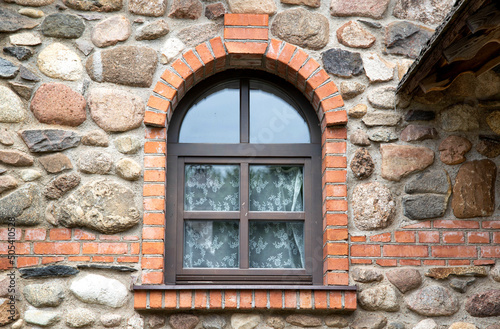 Slika na platnu An old wooden semicircular window lined with bricks in a stone building