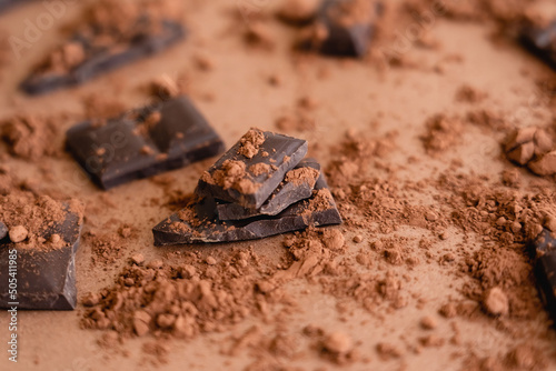 Close up view of cocoa powder on chocolate pieces on brown background.