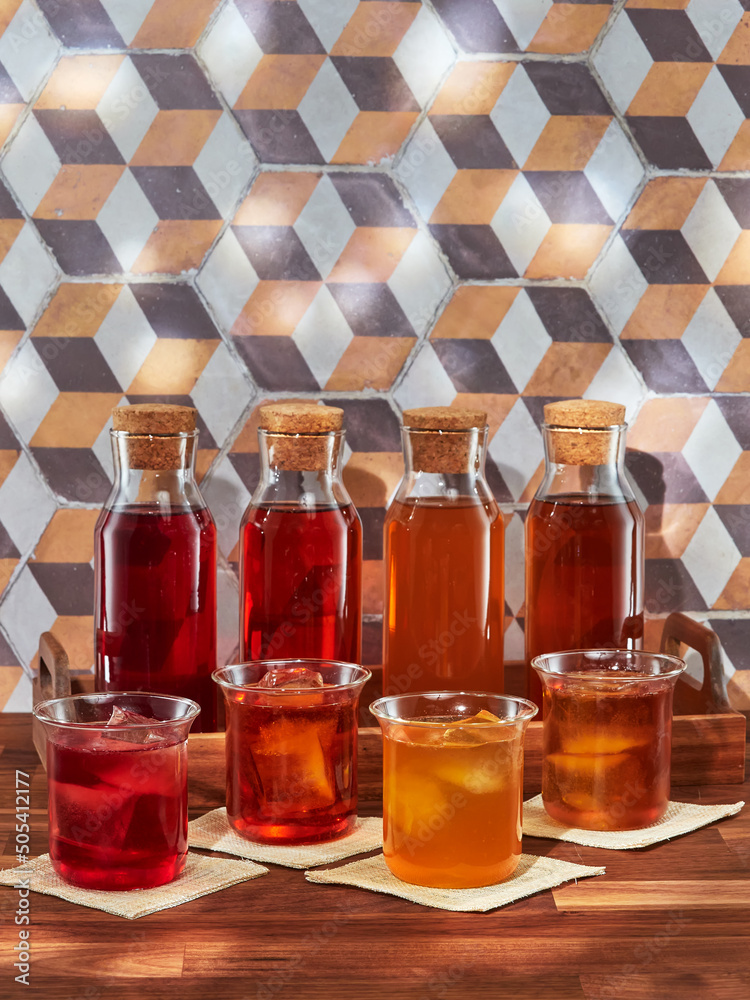 Four bottles and four glasses of cold brew fruit tea, rooibos, green and black, in a wooden tray on a wooden table Four bottles and four glasses of cold brew fruit tea, rooibos, green and black, in a wooden tray on a wooden table
