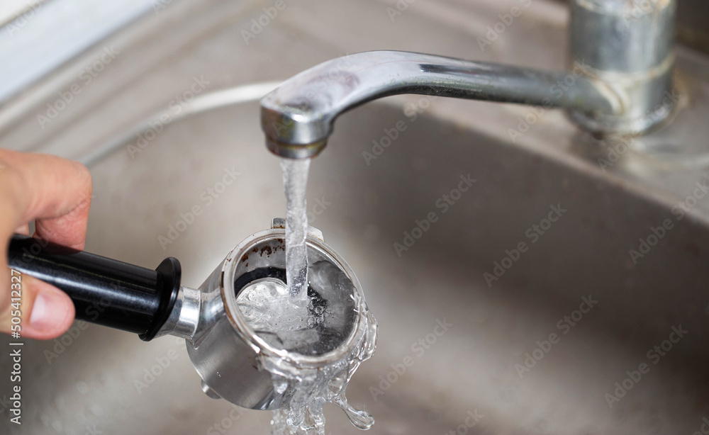 Cleaning the coffee maker's horn under the water of the water tap, close-up. Caring for the coffee machine parts