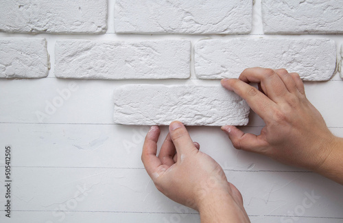 A man glues a white decorative stone in the form of a brick to the wall. Decor element, copy space for text, house renovation photo