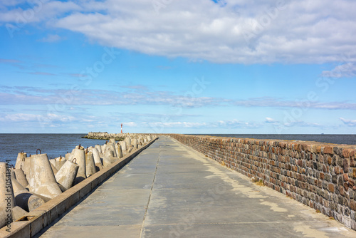 A concrete pier with a brick fence goes into the sea. A clear sunny day and a blue sky with clouds in Baltiysk  Kalinigrad region  Russia  near the Baltic sea.