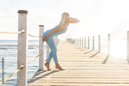 Young beautiful sportive girl training at sunrise over seaside. photo