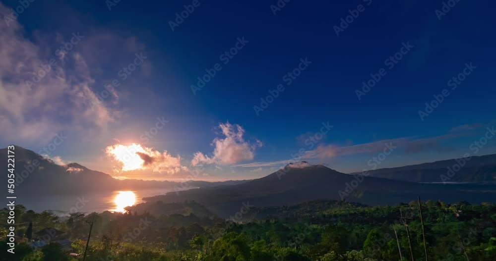 Time lapse of sunset with view on volcanoes and lake on Bali. Clouds are moving fast in blue sky, the sun is setting