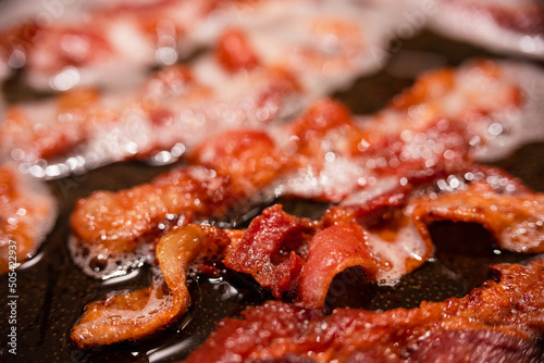 Macro view of appetizing, tasty, bacon slices in a frying pan, close-up, fried meat to scrambled eggs, shallow depth of field
