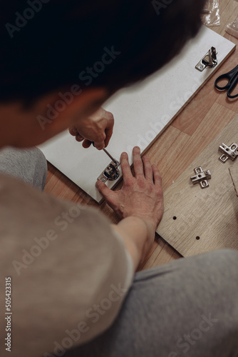 High angle of crop anonymous male assembling wooden cabinet and screwing door hinge with screwdriver 