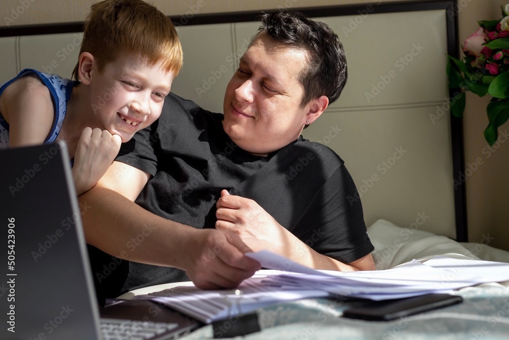 Businessman working on a laptop computer, sitting at home and working with documents, dad working at home. Child son next to father. Freelancing home office concept Businessman working on a laptop computer, sitting at home and working with documents, dad working at home. Child son next to father. Freelancing home office concept