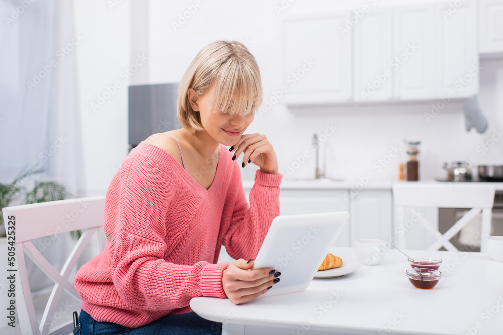 cheerful blonde woman using digital tablet during breakfast. cheerful blonde woman using digital tablet during breakfast.