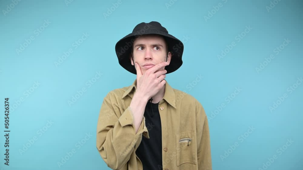 Handsome young man in a shirt stands on a blue background and looks at the camera with a pensive face and thinks Handsome young man in a shirt stands on a blue background and looks at the camera with a pensive face and thinks