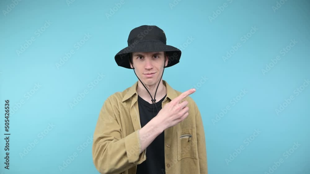 Cute hipster guy in shirt and panama shows finger aside with smile on face on blue background. Cute hipster guy in shirt and panama shows finger aside with smile on face on blue background.