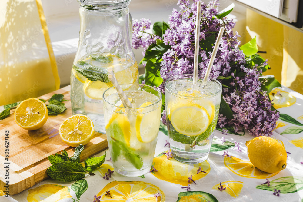 Fototapeta premium Summer scene of lemonade next to a window. Sunlight comes from the window. Lilac flowers on the background