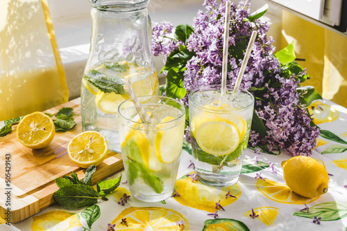 Summer scene of lemonade next to a window. Sunlight comes from the window. Lilac flowers on the background