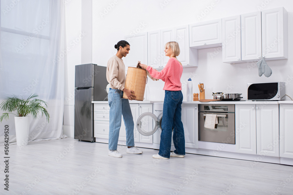 african american man holding basket near washing machine and happy girlfriend. african american man holding basket near washing machine and happy girlfriend.