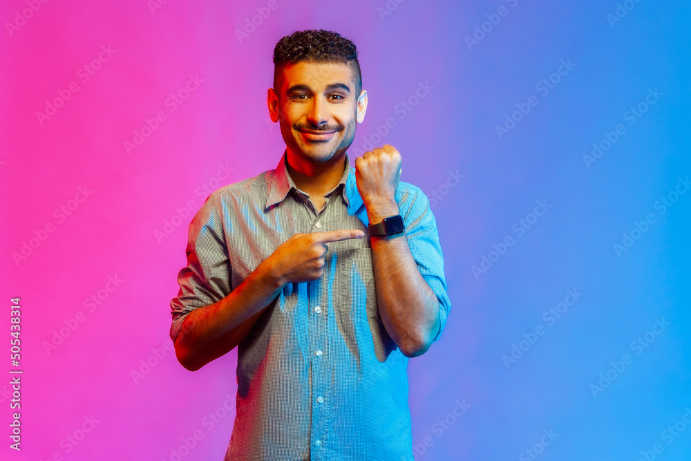 Φωτογραφία Portrait of cheerful punctual man in shirt pointing at wrist watch and smiling, showing smartwatch devise with mock up display