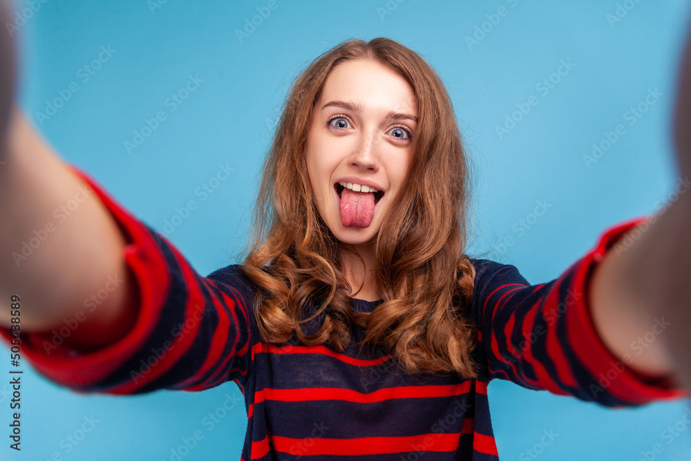 Φωτογραφία Childish woman wearing striped casual style sweater, having funny facial expression taking selfie and showing tongue out, point of view of photo