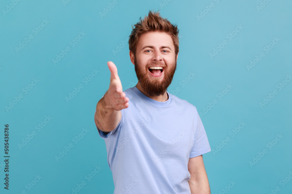 Portrait of happy optimistic bearded man giving hand for handshaking, welcoming partners, job offer, expressing positive emotions and excitement. Indoor studio shot isolated on blue background. Portrait of happy optimistic bearded man giving hand for handshaking, welcoming partners, job offer, expressing positive emotions and excitement. Indoor studio shot isolated on blue background.