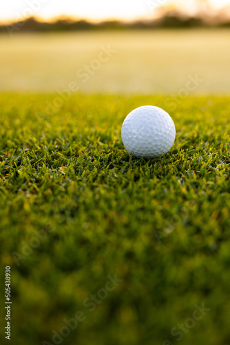 Close-up of white golf ball on lush grassy land at golf course during sunset, copy space