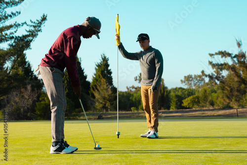 African american young man playing golf with caucasian friend against clear sky at golf course