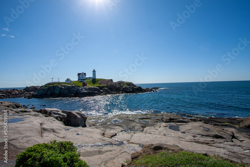 Nubble Lighthouse in Cape Neddick Maine With Rocky Coast Under Morning Sun, Clear Blue, and High Tide photo