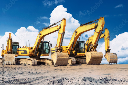 Powerful excavators at a construction site against a blue cloudy sky. Earthmoving construction equipment. Lots of excavators.