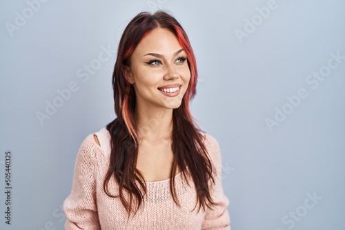 Young caucasian woman wearing pink sweater over isolated background looking away to side with smile on face, natural expression. laughing confident.