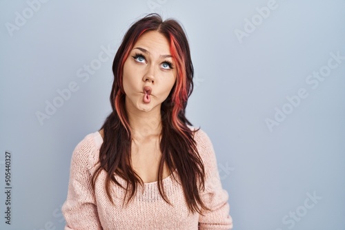 Young caucasian woman wearing pink sweater over isolated background making fish face with lips, crazy and comical gesture. funny expression.