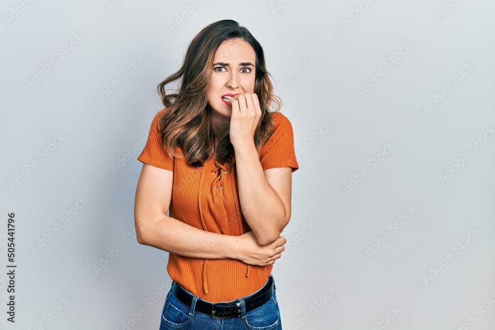 Young hispanic girl wearing casual clothes looking stressed and nervous with hands on mouth biting nails. anxiety problem. Young hispanic girl wearing casual clothes looking stressed and nervous with hands on mouth biting nails. anxiety problem.