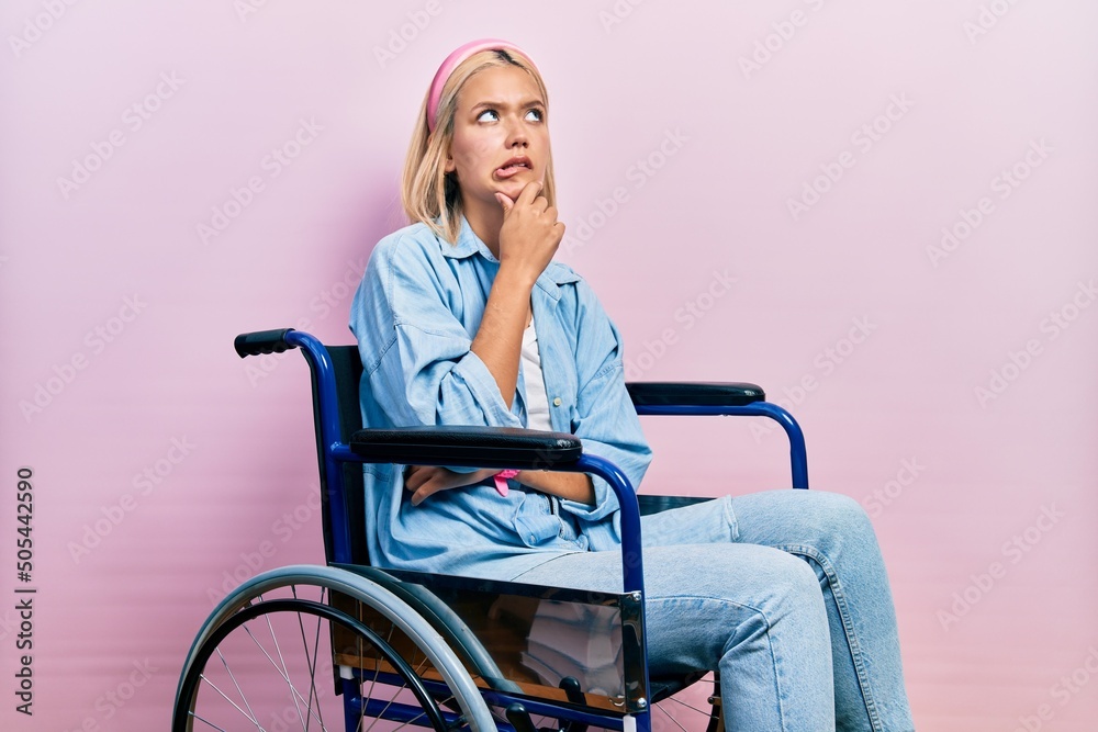 Beautiful blonde woman sitting on wheelchair thinking worried about a question, concerned and nervous with hand on chin Beautiful blonde woman sitting on wheelchair thinking worried about a question, concerned and nervous with hand on chin