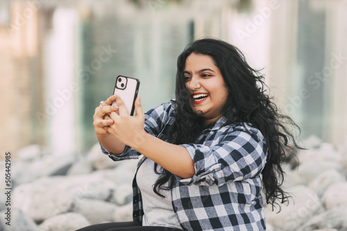 Canvas An Indian girl takes a selfie on her phone while sitting on the embankment while walking in the city