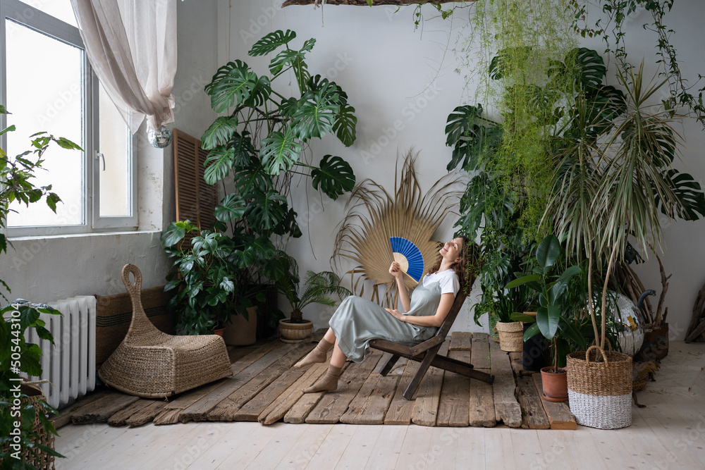 Φωτογραφία Happy young caucasian woman florist relax in home garden breathing fresh air hold paper fan in hand
