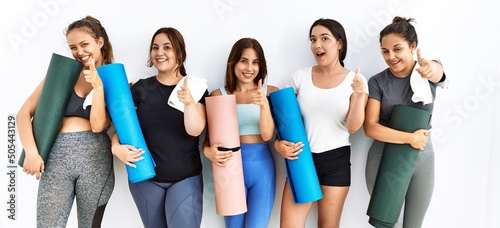 Group of women holding yoga mat standing over isolated background pointing fingers to camera with happy and funny face. good energy and vibes.
