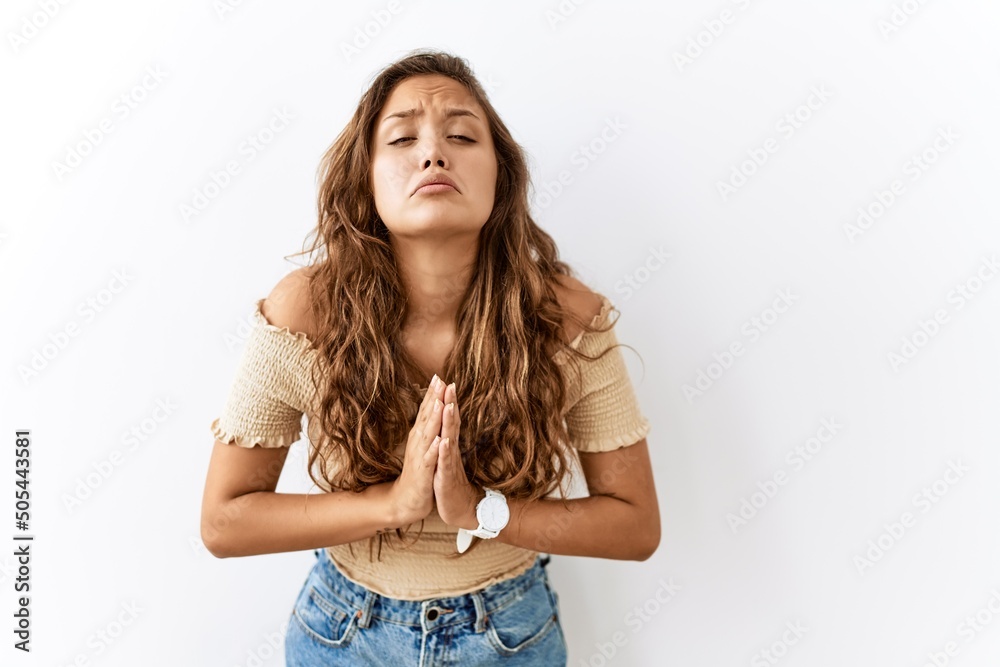 Beautiful hispanic woman standing over isolated while background begging and praying with hands together with hope expression on face very emotional and worried. begging.