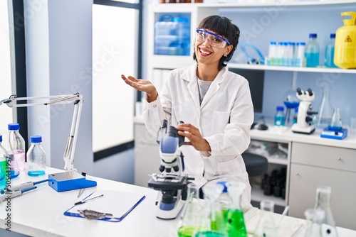 Young hispanic woman working at scientist laboratory celebrating achievement with happy smile and winner expression with raised hand
