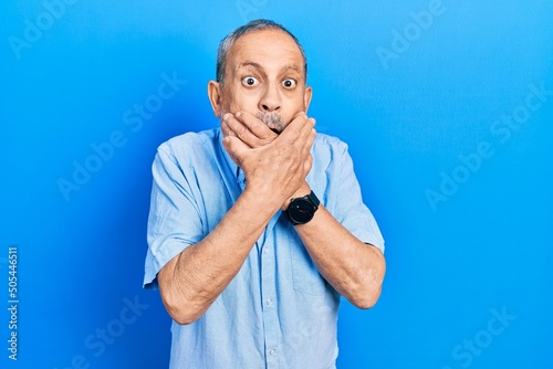 Handsome senior man with beard wearing casual blue shirt shocked covering mouth with hands for mistake. secret concept.