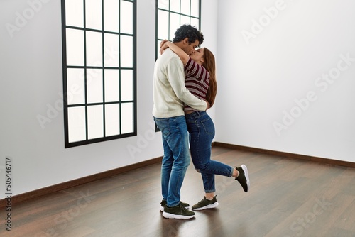 Young hispanic couple kissing and hugging standing at empty new home.